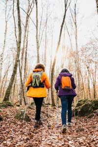 Two senior female friends hiking together through the forest in autumn